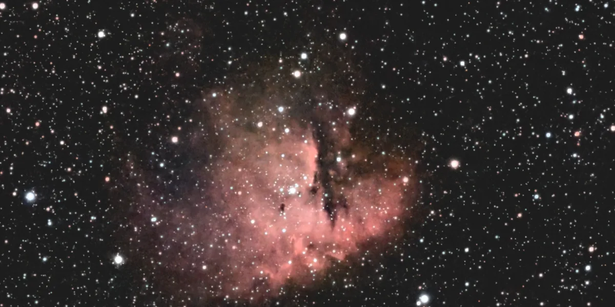 The Pacman Nebula after the Darkroom: bright pink gas, dark dust pillars and a cluster of young stars, on a dark, even sky.
